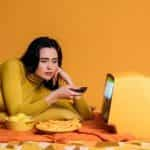 A woman in yellow watching a television, with snacks.