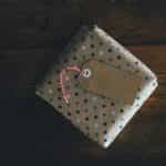 A small present in gift wrapping lying flat on a table, with a small tag on top of it.