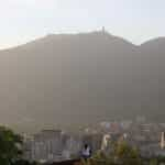 A person in a white t-shirt stands overlooking Caracas, Venezuela, with a hazy mountain in the background.