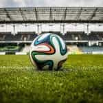 A football on a grass pitch in a stadium.