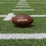 A classic brown American football sitting on a grass pitch at the start of a big game.