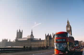 A red bus passing across the bridge in front of Westminster in London, UK.